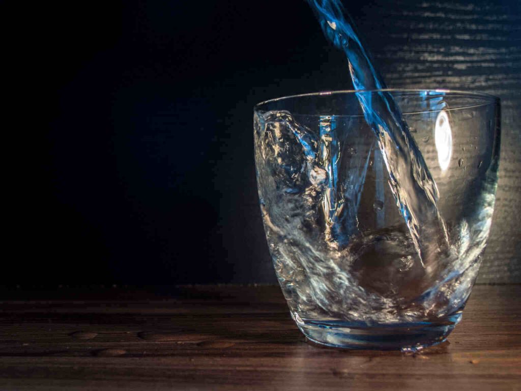 pouring water into a glass on wooden benchtop